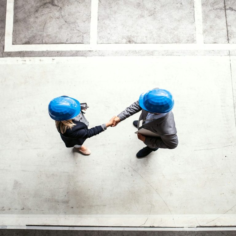 Bild von unsplash Zwei Personen in Schutzhelmen schütteln sich die Hände in einem modernen Raum.